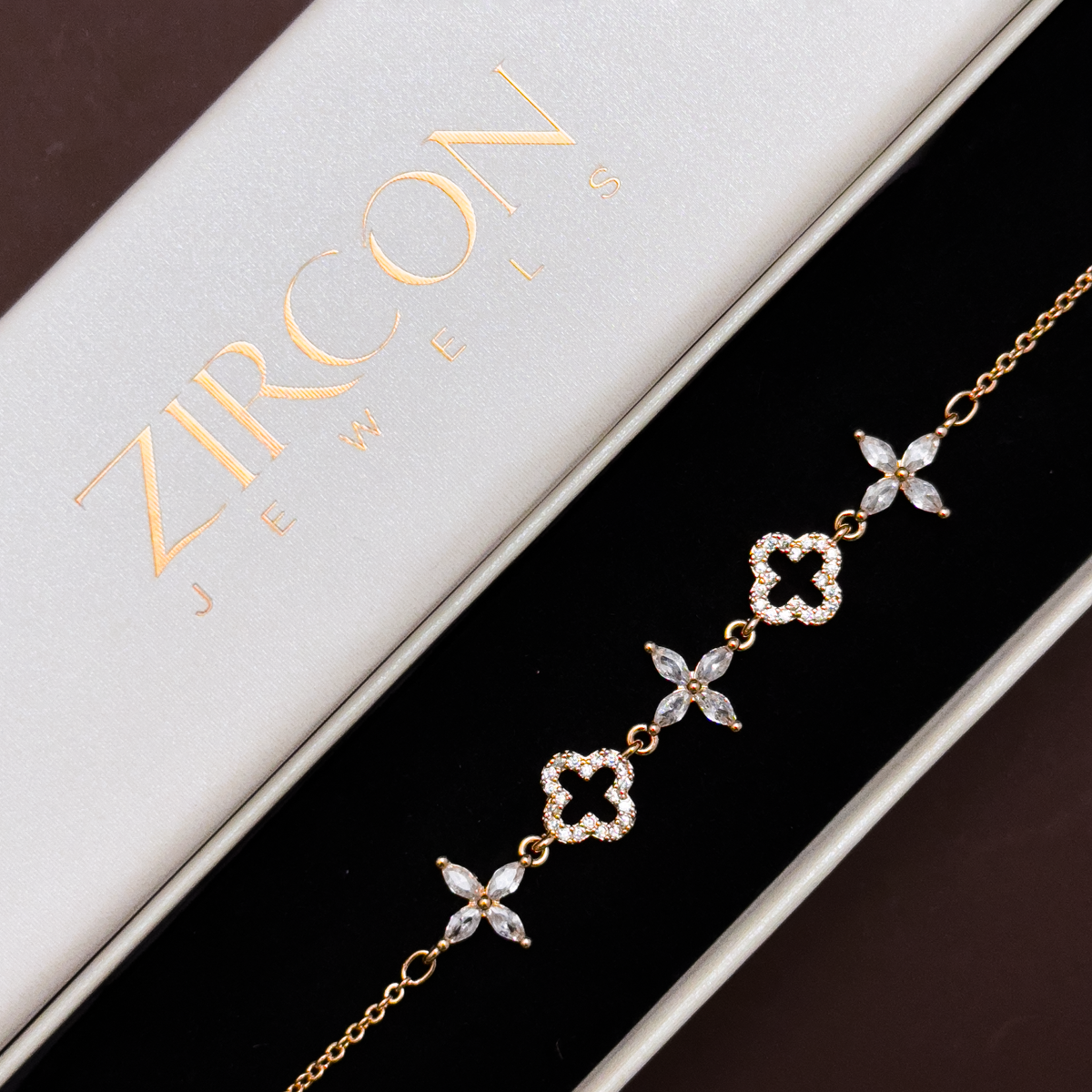 Gold bracelet with clover and floral designs on a Zircon branded box