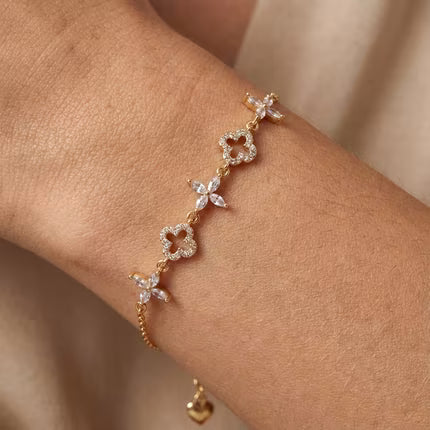 Gold-plated clover charm bracelet with pavé clover links and marquise-cut floral stones, worn on the wrist.