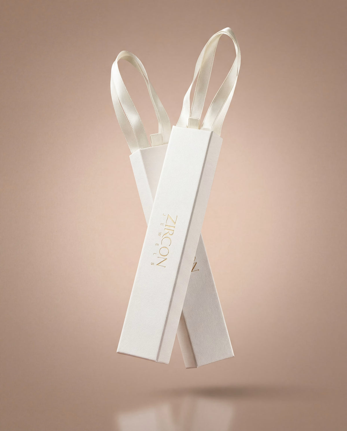 Two white Zircon jewelry gift boxes with satin ribbon pulls on a soft beige background.