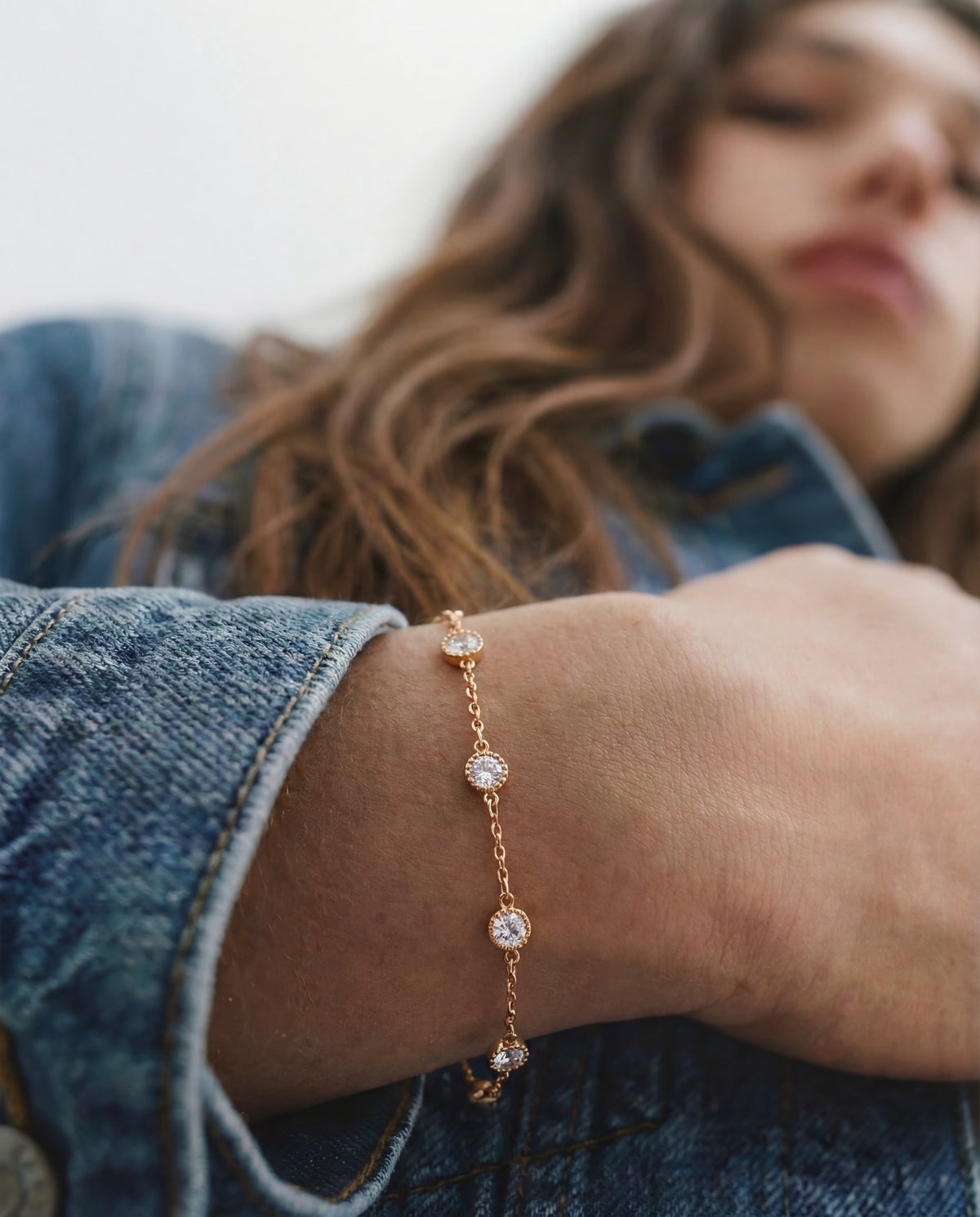 Rose gold-plated station bracelet with bezel-set round clear stones worn on the wrist, styled with a denim jacket.