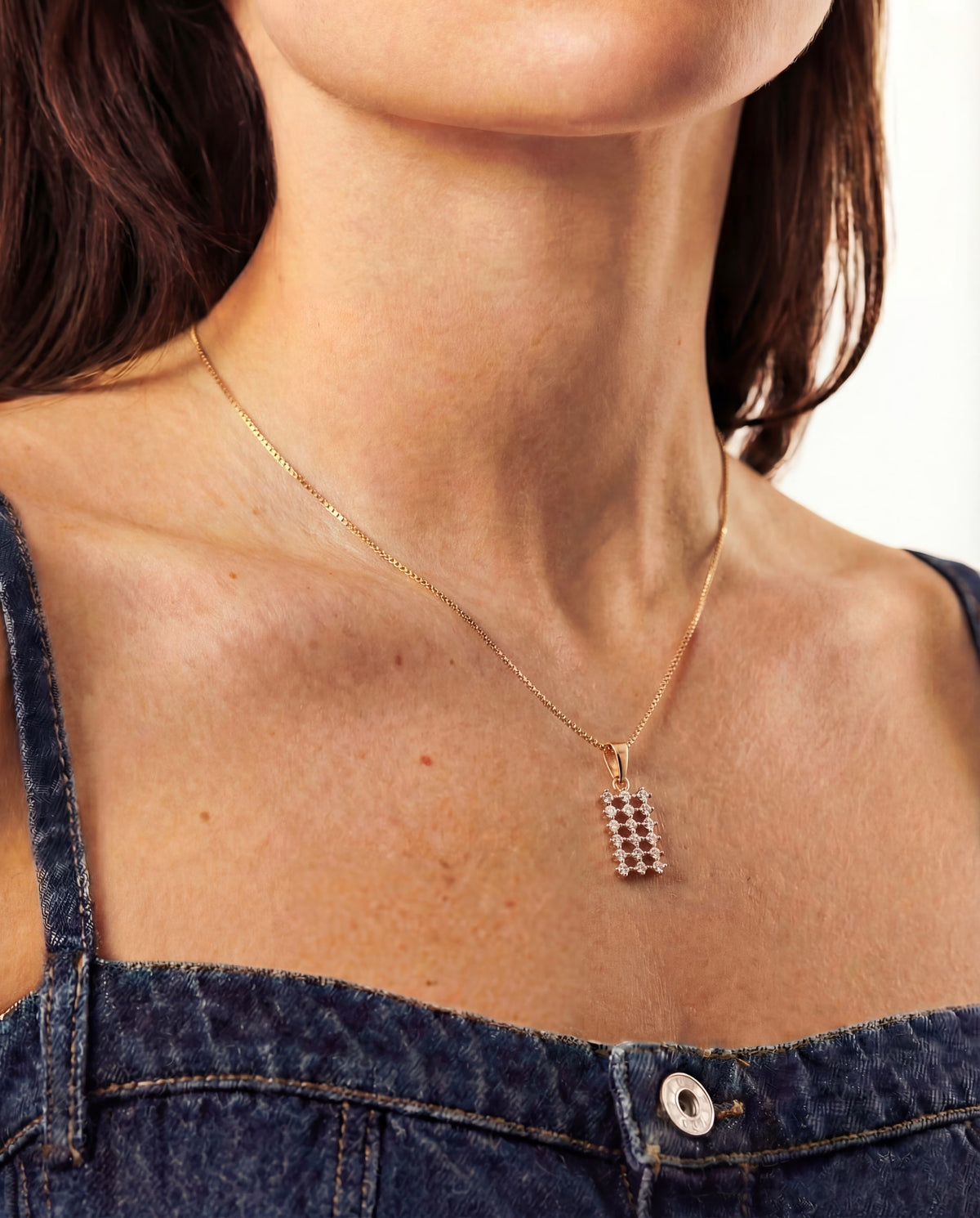 Close-up of a person wearing a gold-plated necklace with a rectangular pendant.