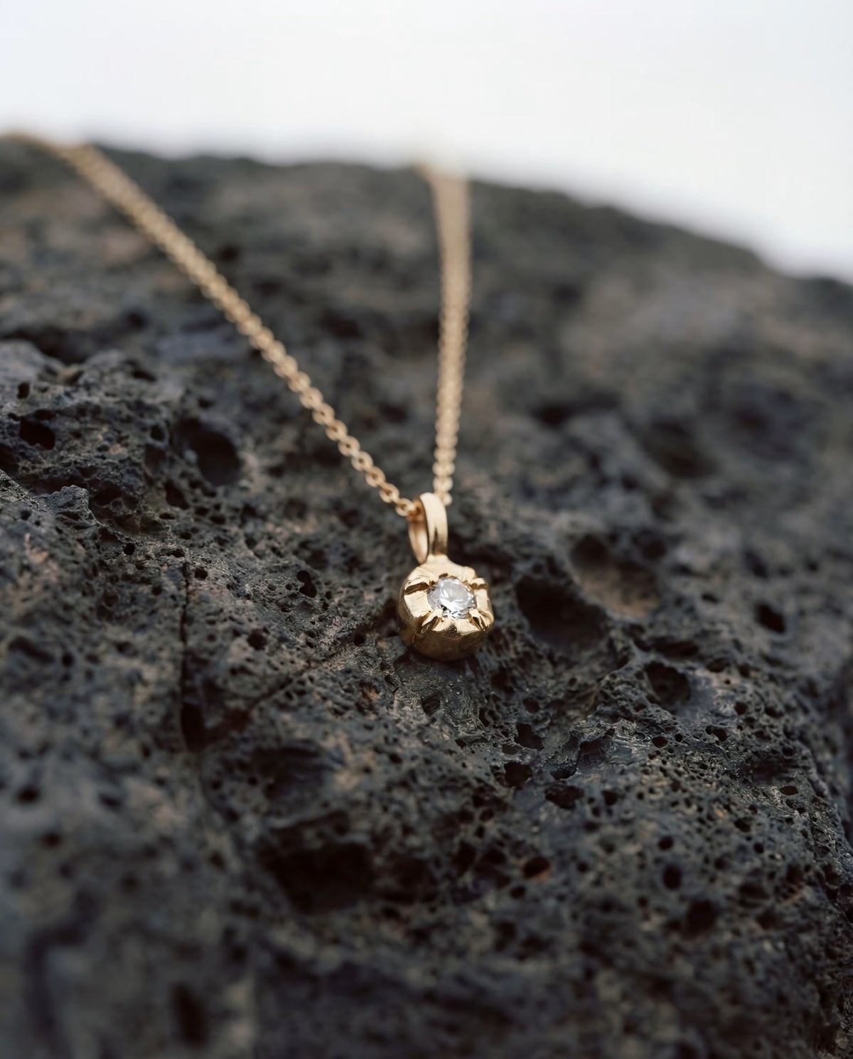 Gold-plated solitaire pendant necklace with a single clear stone in a textured setting.